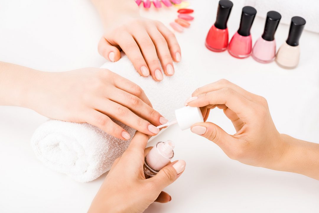 girl holding hands on towel while manicurist applying nail polish